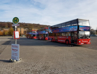 Parkplatz mit mehreren roten Hop-on-Hop-off-Doppeldeckerbussen der Firma City Tour neben einer Bushaltestelle.